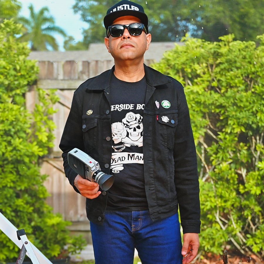 Chuck Livid holding a camera, wearing a denim jacket and sunglasses